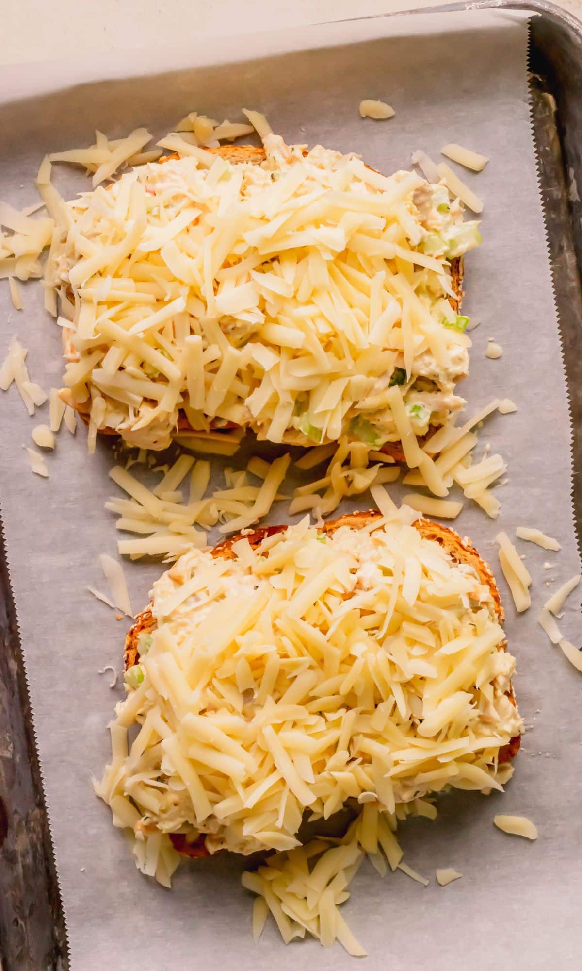 Tuna melts topped with shredded cheese before baking.