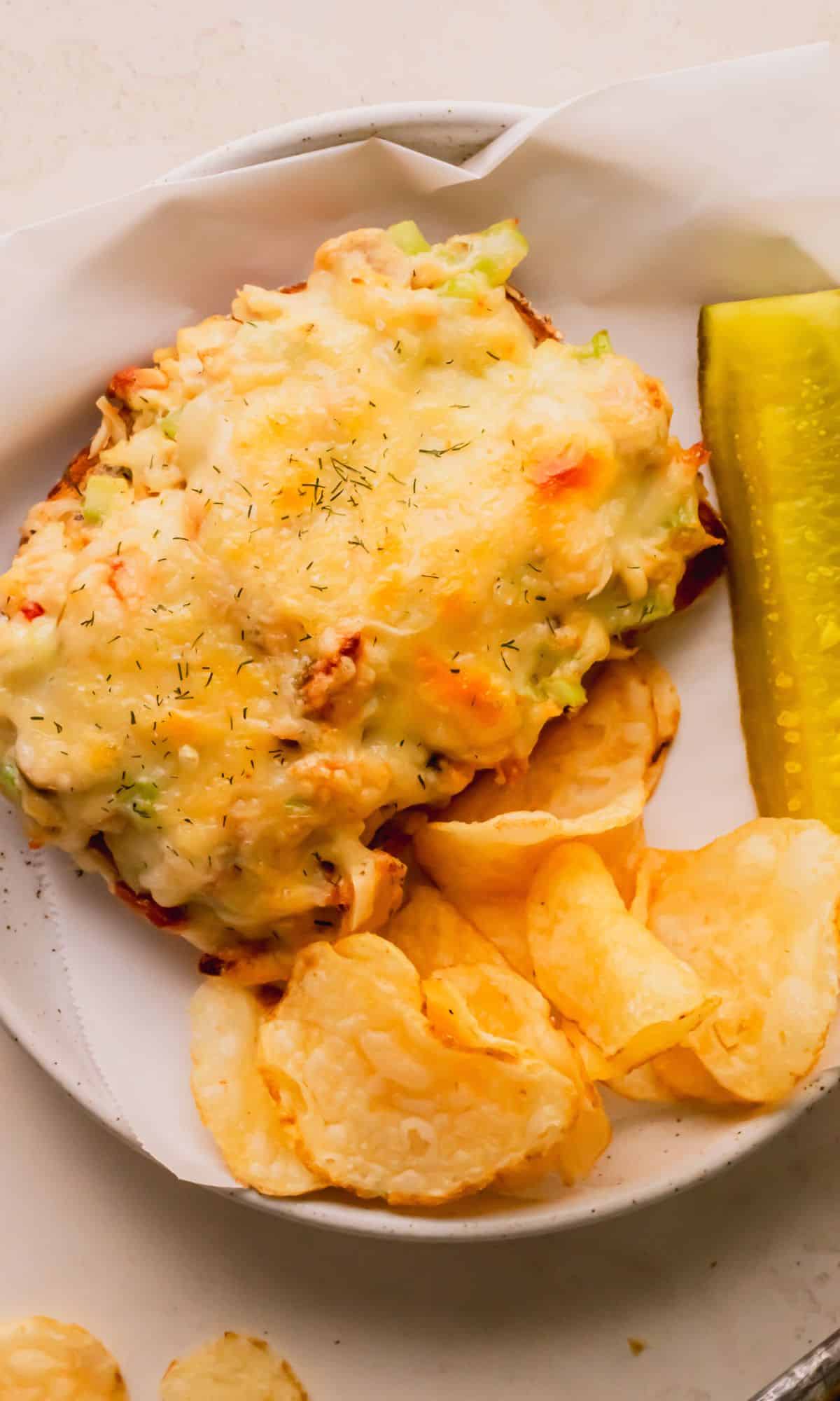 Tuna melt on a plate with chips and a pickle.