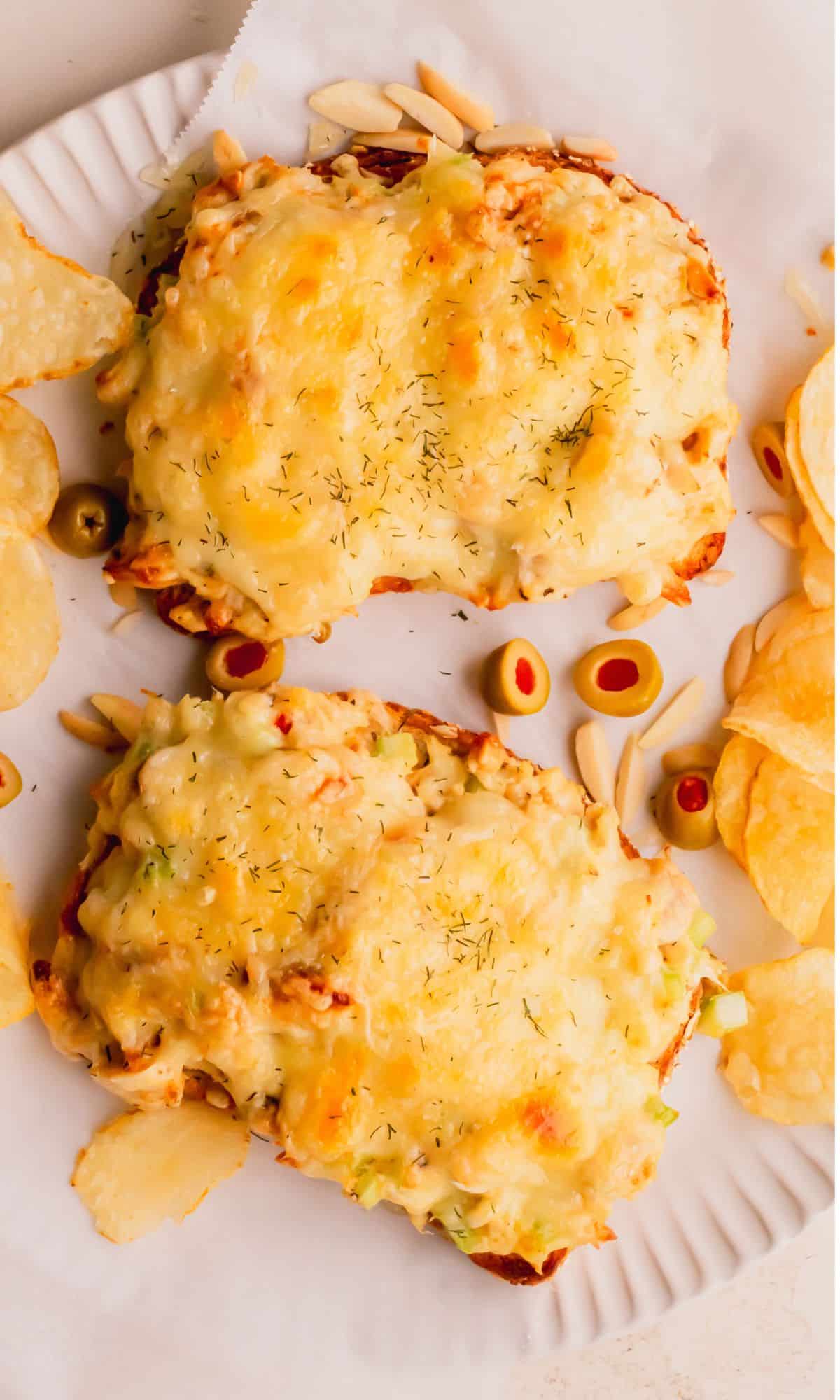Two tuna melts on a plate surrounded by olives and chips.