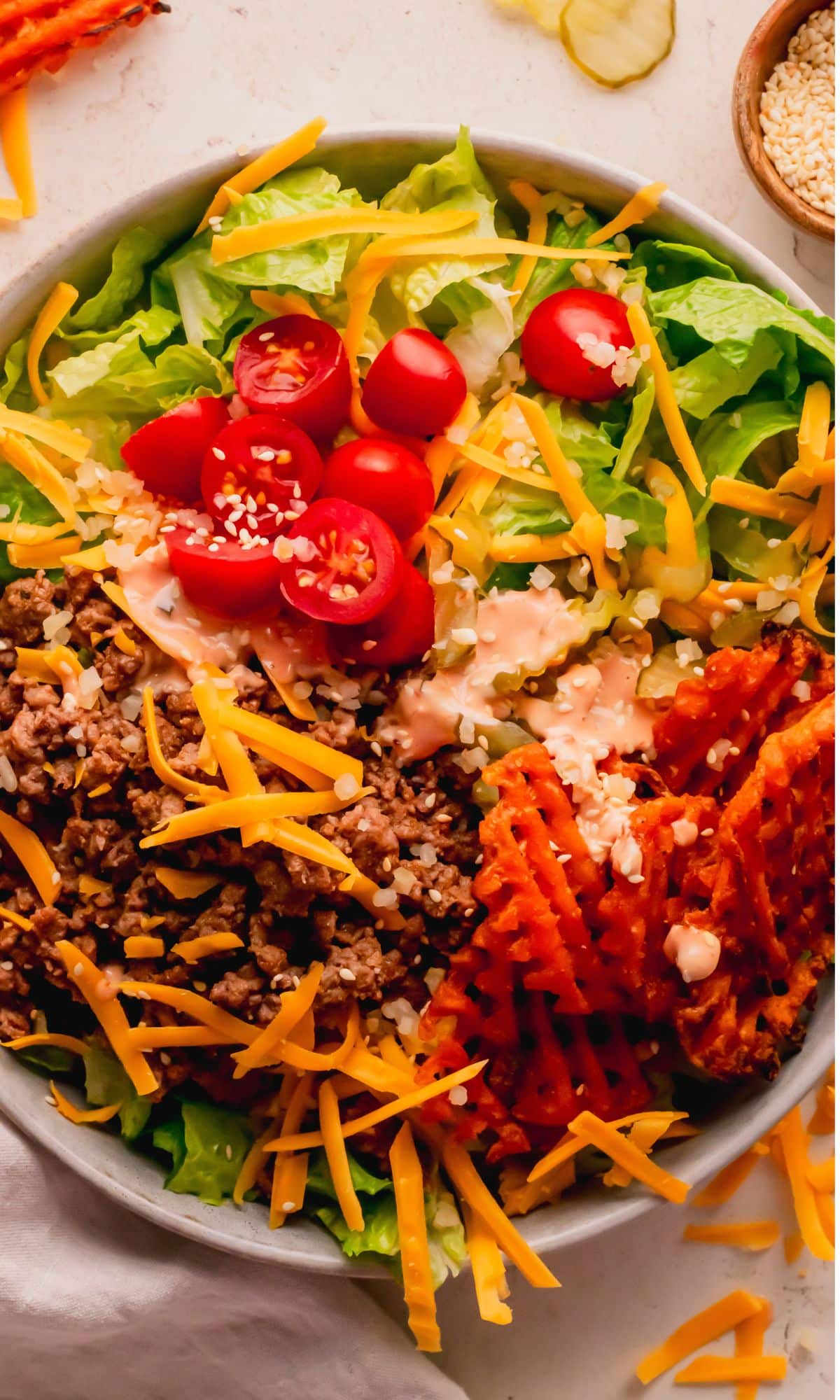 A cheeseburger salad topped with cheese and sweet potato fries.