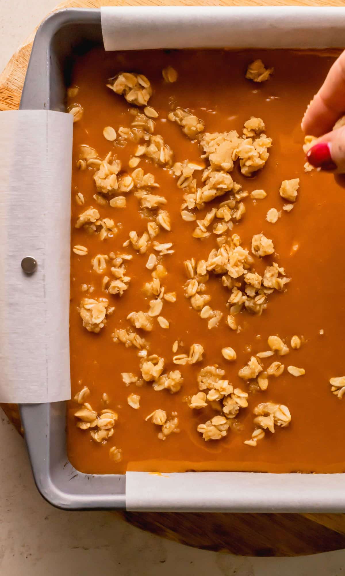 Sprinkling oat mxiture on top of caramel layer in pan.