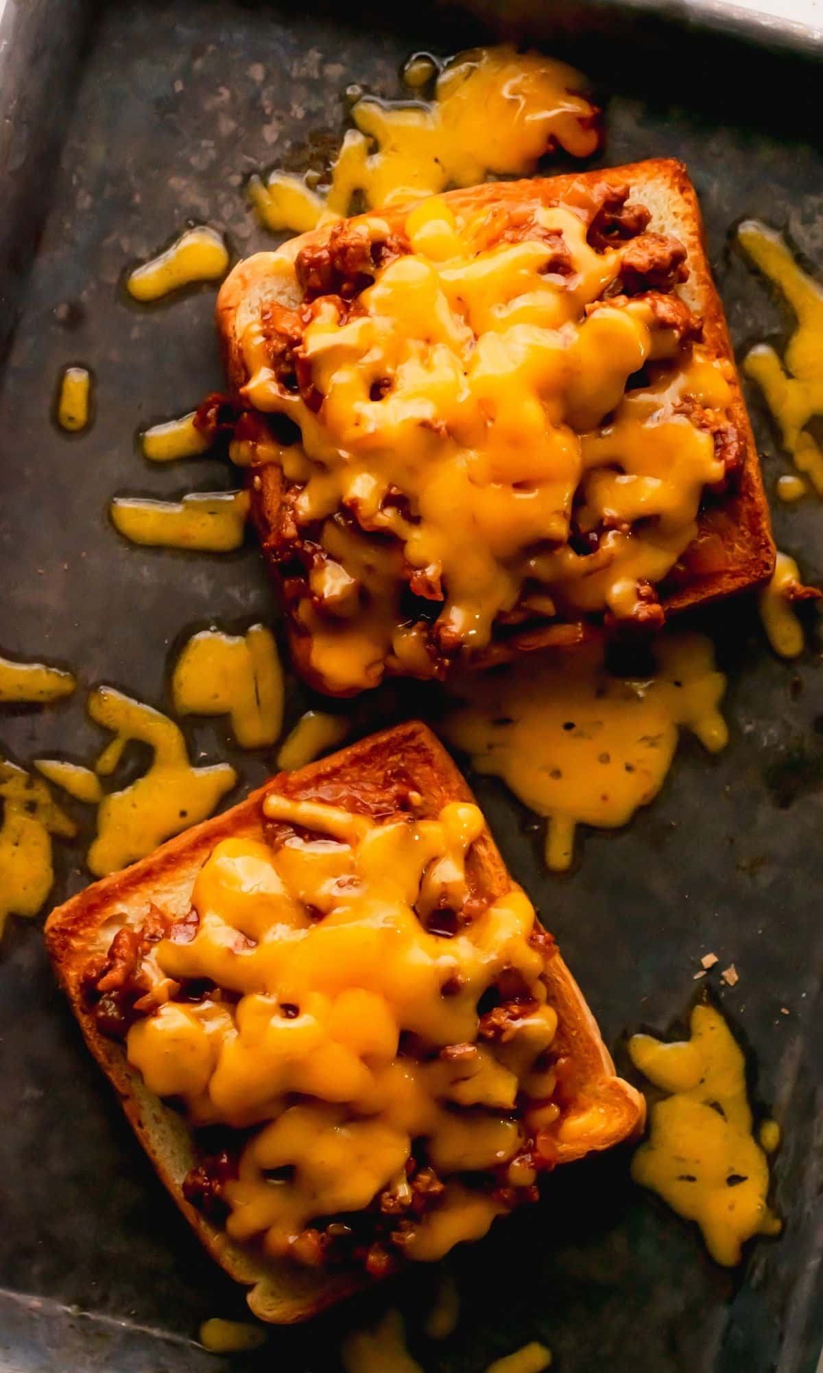 Two open-faced sloppy joes topped with melted cheese on a baking sheet.