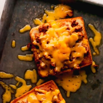 Two open-faced sloppy joes topped with melted cheese on a baking sheet.