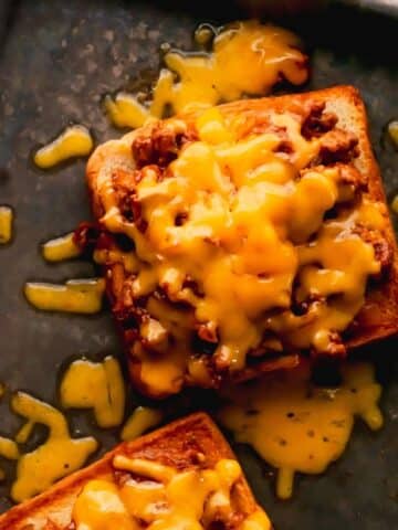Two open-faced sloppy joes topped with melted cheese on a baking sheet.