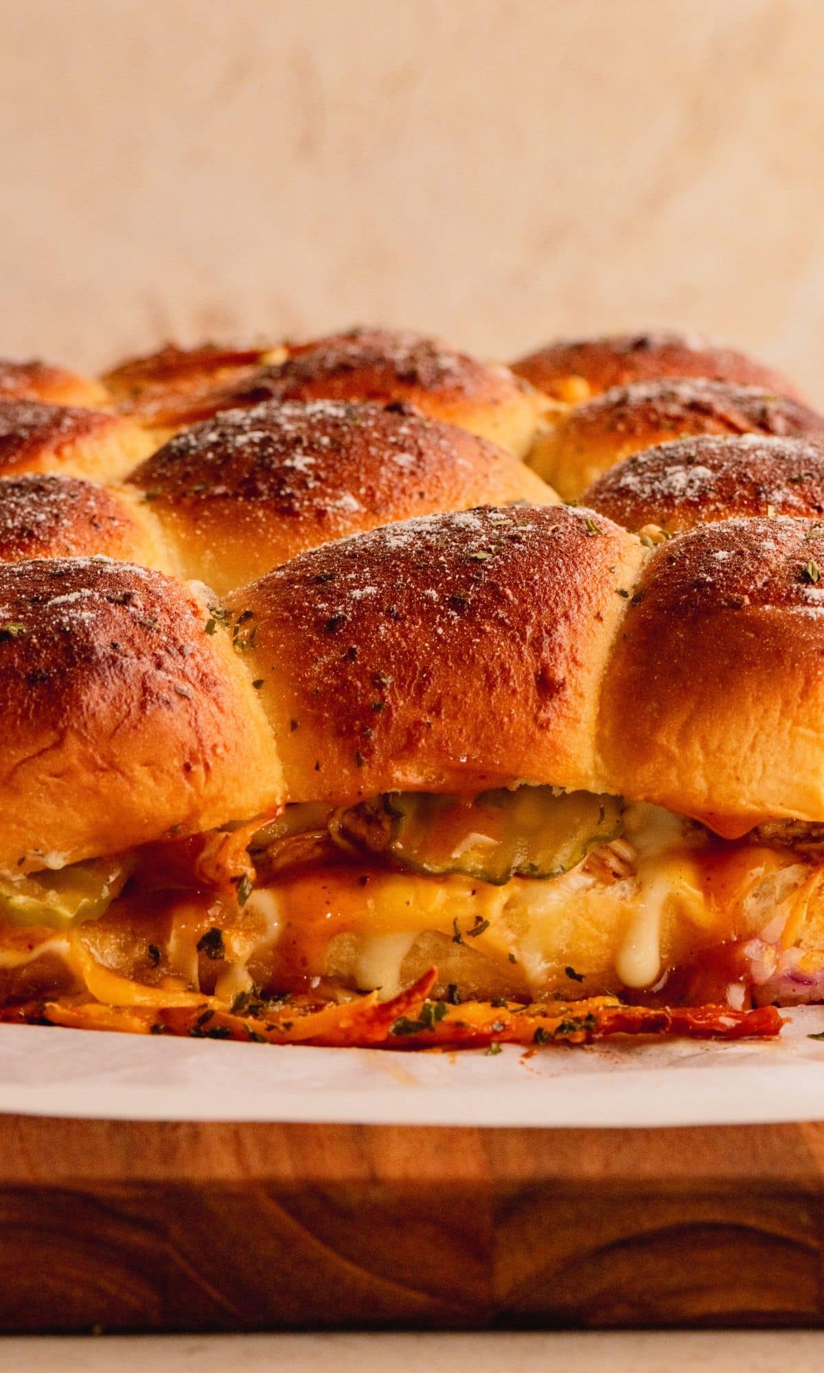 A side view of chicken sliders showing melted cheese, pickes and BBQ sauce.