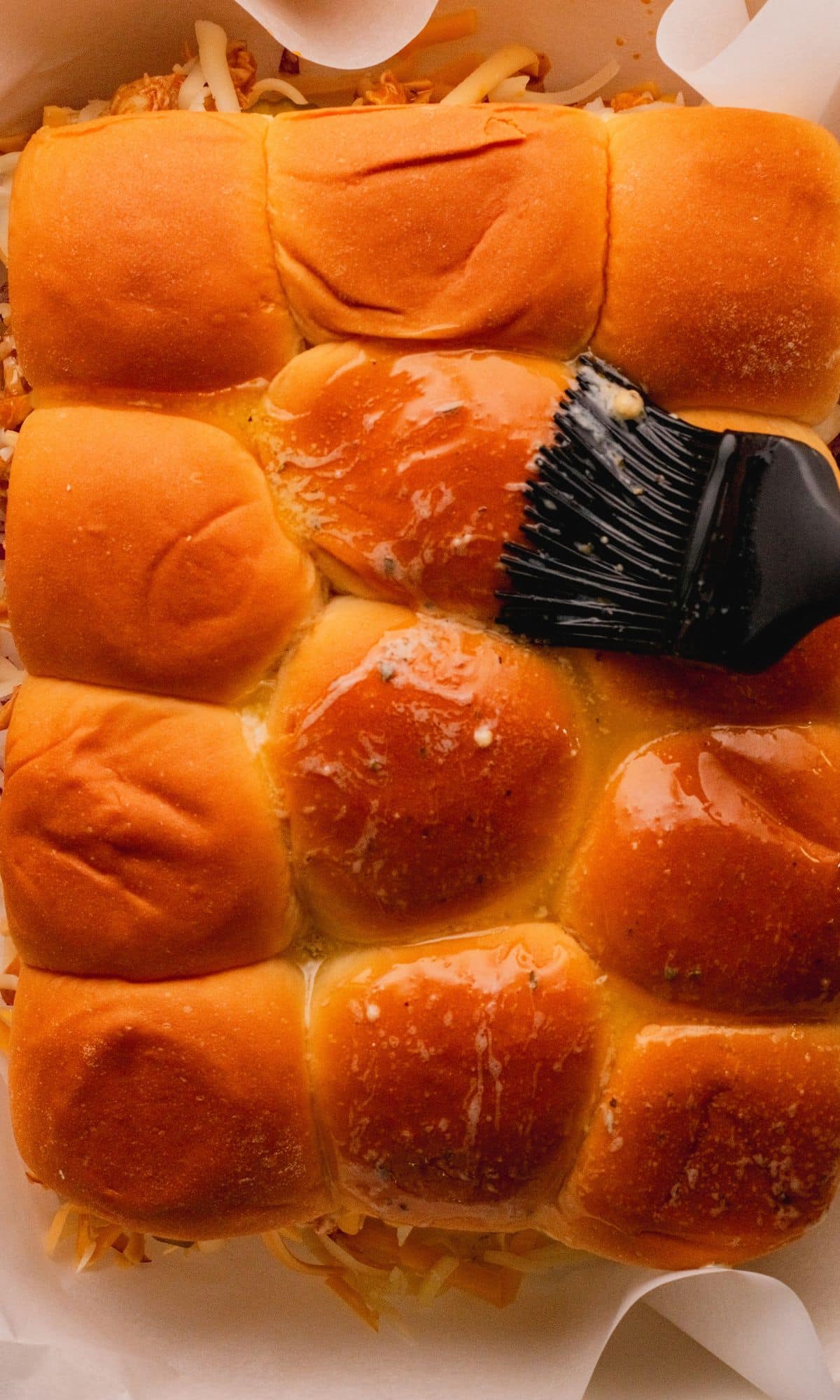 Brusing melted butter on slider bun tops.