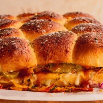 A side view of chicken sliders showing melted cheese, pickes and BBQ sauce.