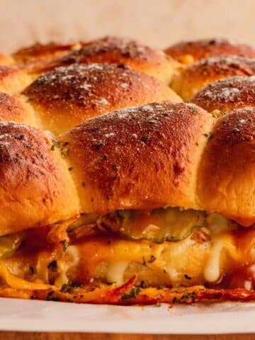 A side view of chicken sliders showing melted cheese, pickes and BBQ sauce.